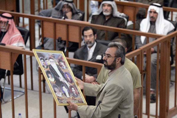 BAGHDAD, IRAQ - DECEMBER 5: Witness Ahmad Hassan Mohammed Al Dujaili, holding pictures of deceased relatives killed in Dujail, testifies in open court during the trial of former Iraqi President Saddam Hussein held under tight security in the heavily fortified Green Zone, December 5, 2005 in Baghdad, Iraq. Saddam and seven others face charges that they ordered the killing of nearly 150 people in the mainly Shiite village of Dujail, north of Baghdad, after a failed attempt on the former dictators life in 1982 . (Photo by David Furst-pool/Getty Images) *** Local Caption *** Mohammed Al Dujaili
